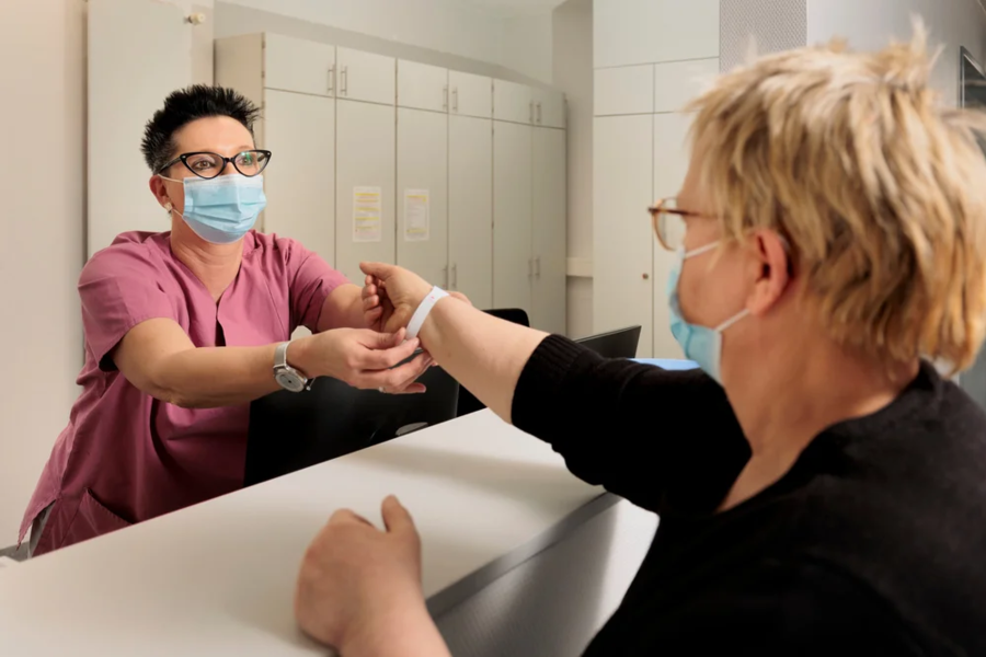 Pflegekraft in rosa Arbeitskleidung legt einem Patienten am Empfang eine Armbanduhr an