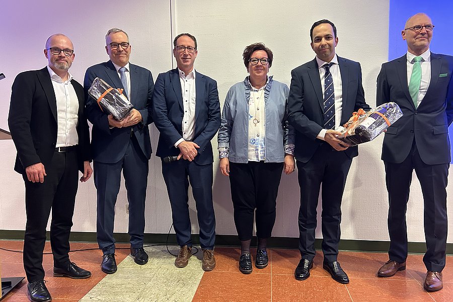 Sechs Personen in formeller Kleidung stehen nebeneinander, zwei halten Geschenkkörbe