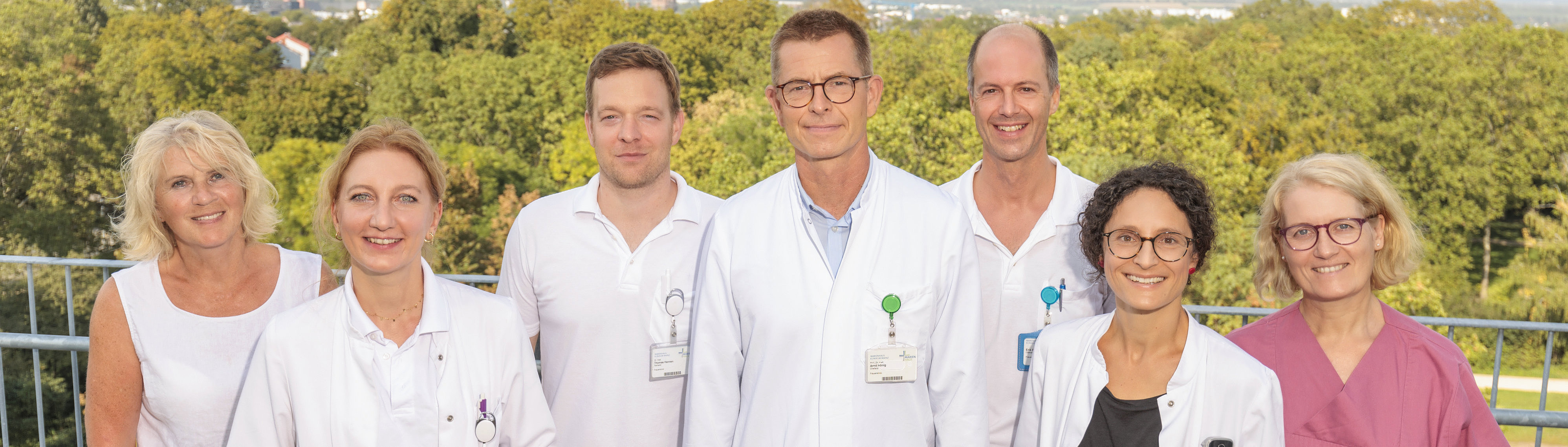 Gruppe von Medizinern in weißen Kitteln auf einer Terrasse mit Blick auf die Landschaft.