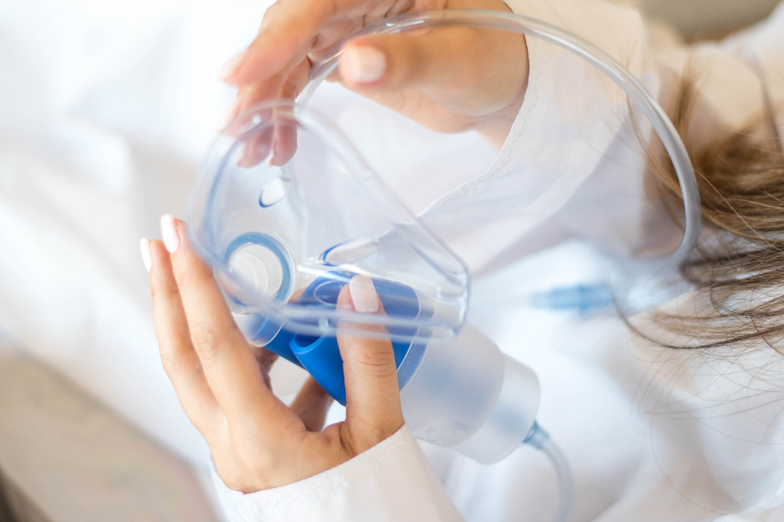 Person hält ein transparentes Sauerstoffinhalationsgerät mit blauen Ventilen