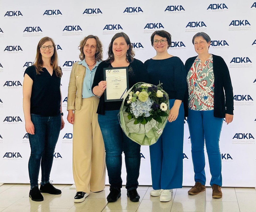 Fünf Frauen stehen vor einer Wand mit dem ADKA-Logo, eine hält eine Urkunde, eine andere einen großen Blumenstrauß.
