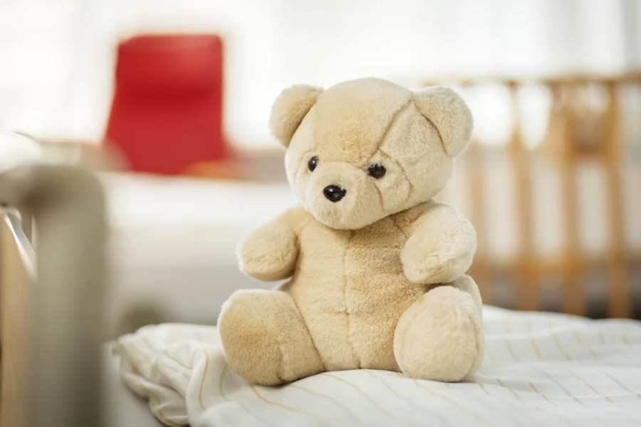 Beiger Plüschbär sitzt auf einer gestreiften Decke. Der Bär hat schwarze Augen und eine kleine Nase.