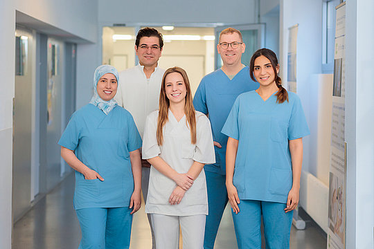 Fünf Personen in medizinischer Arbeitskleidung stehen in einem Krankenhausflur