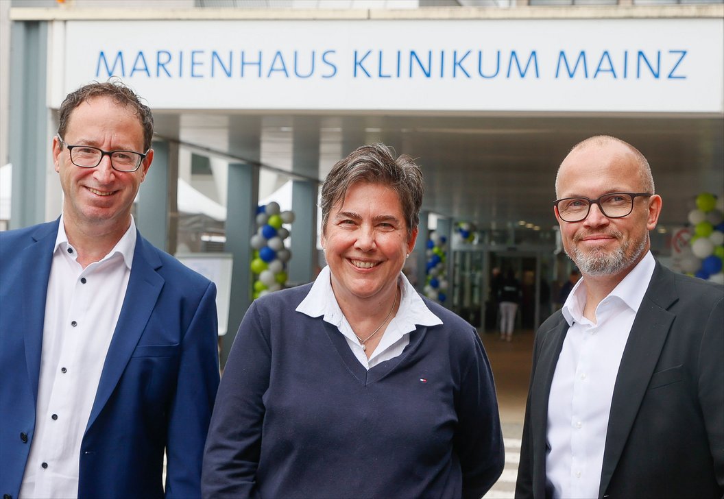 Drei Personen stehen vor dem Eingang des Marienhaus Klinikums Mainz, erkennbar am Schriftzug über dem Eingang.