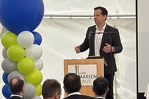 Oberbürgermeister Nino Haase in dunklem Anzug hält Rede an Rednerpult mit Schriftzug 'MARIEN HAUS' vor Publikum in Zelt mit blau-weißer und grüner Ballongirlande