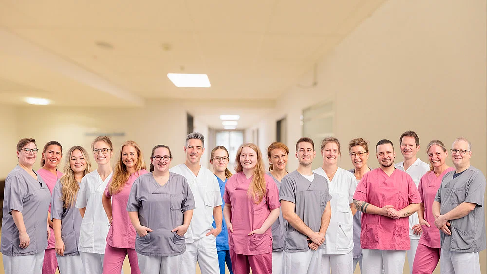 Gruppe von medizinischem Personal in bunten Kitteln steht in einem Krankenhausflur