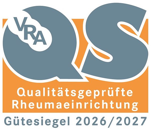 Orangenes Gütesiegel mit den großen Buchstaben Q und S, darin die Buchstaben VRA, darunter der Text 'Qualitätsgeprüfte Rheumaeinrichtung Gütesiegel 2026/2027'